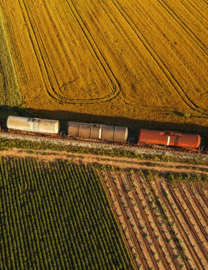 Tank railcars traveling through farm fields.